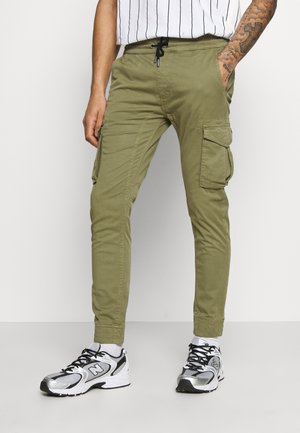 Khaki cargo pants with a tapered fit, drawstring waist, and multiple side pockets; smooth, durable fabric. Worn with black-and-white sneakers.