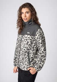 Fuzzy fleece jacket with gray shoulders, white base, and black leopard spots. Features a zip front and side pockets. Textured surface.
