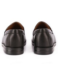 Mocassini in pelle nera con punta rotonda, texture liscia e dettagli di cucitura minimi; rivestimento interno sottile e testurizzato e suola piatta in gomma.