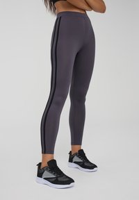 Szare legginsy z czarnymi paskami bocznymi, wykonane z elastycznego materiału. Połączone z czarno-szarymi butami sportowymi z siateczkowymi akcentami.