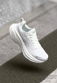 Hvide sportssko med en glat, tekstureret overdel, hævet sål og perforerede detaljer. Har snørebånd og et minimalistisk design.