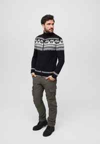 Suéter negro con cremallera y patrón fair isle blanco, con puños acanalados, combinado con pantalones cargo oliva y botas negras con cordones.