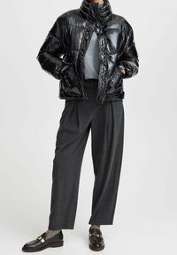 Doudoune noire avec finition brillante, col haut, fermeture éclair, assortie à un pull gris et un pantalon gris foncé ajusté, mocassins noirs.