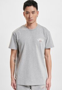 Szara bawełniana koszulka z okrągłym dekoltem, krótkimi rękawami i nadrukowanym logo "UNFAIR" w białym i czerwonym kolorze na klatce piersiowej. Gładka tekstura.