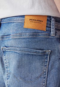 Modré džínové kalhoty s koženou nášivkou s nápisem "JACK & JONES" v pase, s zadními kapsami a detaily šití.