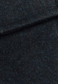 Tessuto di lana scuro con una superficie texture, caratterizzato da un colore blu-nero profondo. Il materiale appare denso con una finitura morbida e pelosa.