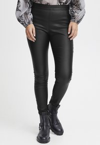 Svarta syntetiska läderleggings har en elegant design med hög midja, i kombination med ankelhöga svarta stövlar prydda med metallaccenter.