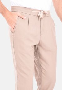 Pantaloni beige con vita regolabile, pieghe frontali, tasche laterali e una texture liscia. Adatti per un abbigliamento casual o rilassato.