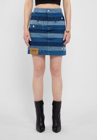 Denim svārki ar maiņām ziliem un gaiši ziliem horizontāliem svītrām, sudraba detaļām un brūnu uzlīmi ar "Moschino Jeans" uz priekša.
