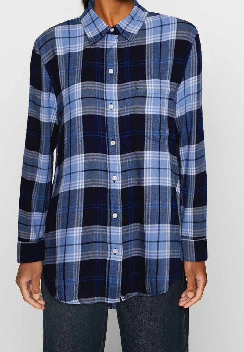 Long-sleeve, button-up shirt in blue and navy plaid. Features a collar, front buttons, and side pockets. Made of soft, checkered fabric.