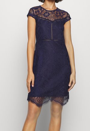 Navy-blaues Spitzenkleid mit kurzen Ärmeln, das ein Blumenmuster und einen gewellten Saum aufweist. Durchsichtiges Spitzenoberteil mit taillierter Passform und strukturiertem Stoff.