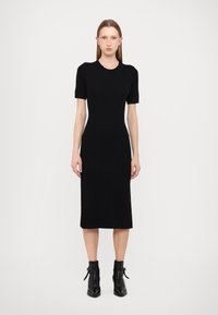 Black knitted dress with short sleeves, fitted silhouette, knee-length hem, and textured pattern; paired with black ankle boots.