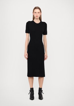 Black knitted dress with short sleeves, fitted silhouette, knee-length hem, and textured pattern; paired with black ankle boots.