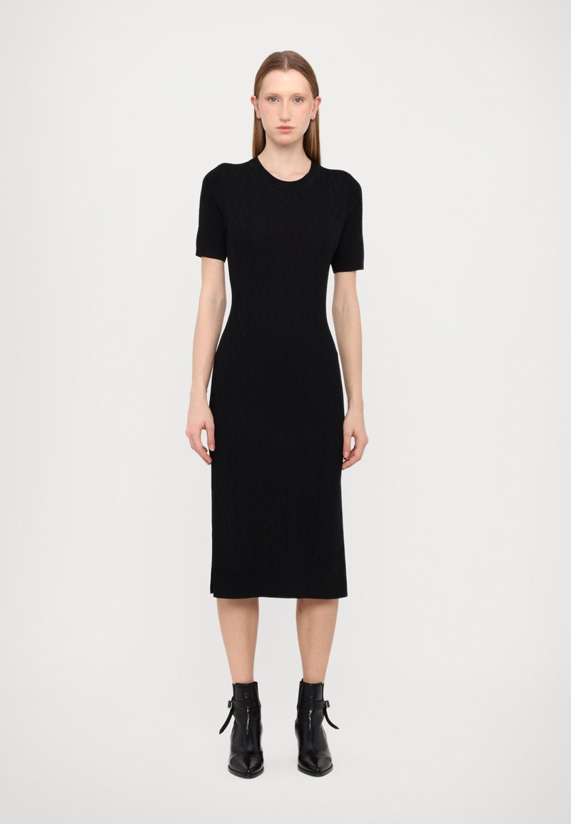 Black knitted dress with short sleeves, fitted silhouette, knee-length hem, and textured pattern; paired with black ankle boots.