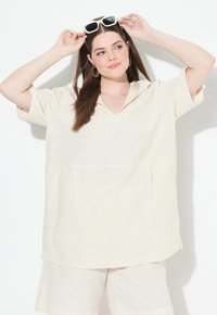 Camisa oversized de color beige claro con finas rayas verticales, mangas cortas y escote en forma de V, combinada con pantalones cortos a juego de tela similar.