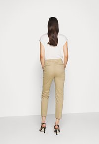 Beżowe spodnie o zwężanych nogawkach wykonane z lekkiego materiału, z tylnymi kieszeniami i dopasowaną talią. Połączone z czarnymi sandałami na wysokim obcasie.