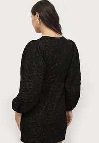 Abito nero con motivo floreale testurizzato, maniche a sbuffo e vita aderente. Chiusura con zip sul retro per facilità di indossamento.