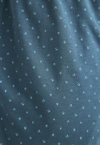 Baumwollstoff in dunklem Teal mit einem kleinen, hellblauen, verstreuten Punktmuster. Glatte Textur, atmungsaktives Material und durchgehend einheitliche Farbe.