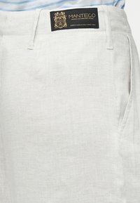 Ανοιχτό γκρι λινά παντελόνια με λείο υφής, πλαϊνή τσέπη και μαύρη ετικέτα με χρυσά γράμματα στη μέση.