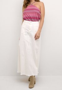 Vit denimmaxikjol med en lätt fransad nederkant, i kombination med en mönstrad rosa halterneck-top med böjda linjer och en avslappnad passform.