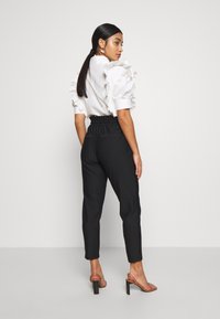 Blusa branca com mangas volumosas, combinada com calças pretas com riscas verticais, apresentando uma cintura elástica e perna ajustada. Sapatos de salto aberto.