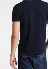 Tmavě modré bavlněné tričko s krátkým rukávem, kulatým výstřihem a hladkým povrchem. Na zadní straně nejsou viditelné žádné vzory ani akcenty.