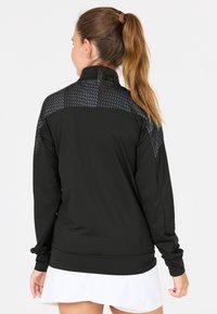 Svart långärmad träningsjacka med en texturerad svart panel på övre delen av ryggen. Slätt tyg med åtsittande ärmslut och ståkrage.
