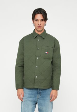 Groene gewatteerde jas met een knoopsluiting aan de voorkant, een enkele borstzak en een klein, multicolor logo. Gestyled met blauwe denim jeans.