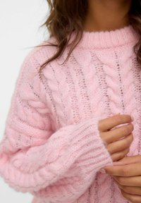 Pull en maille torsadée rose avec un col montant, une texture douce et des manches longues avec des bords côtelés. Motif de fil épais et fin remarquable.