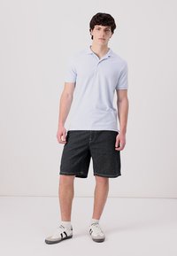 Světle modré polo tričko s krátkým rukávem zkombinované s černobíle pruhovanými šortkami. Model má na sobě bílé a černé sportovní boty. Jednoduchý design.