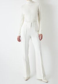 Jersey blanco ajustado con cuello alto y un tejido texturizado, adornado y combinado con pantalones blancos de cintura alta que presentan un corte entallado y piernas acampanadas.