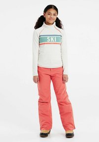 Maglia da sci a maniche lunghe off-white con strisce turchesi e corallo, con la scritta "SKI". Abbinata a pantaloni da neve corallo vivaci e stivali neri.