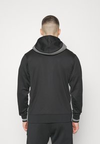 Sweat à capuche noir avec une doublure grise, design ajusté, texture douce et accents côtelés aux poignets et à l'ourlet. La vue arrière ne montre aucun logo.