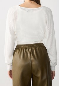 Vit, texturerad stickad topp med en croppad design och samlade ärmar, ihopparad med olivgröna, glänsande, plisserade byxor med hög midja.