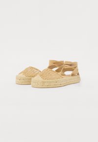 Sandali espadrillas intrecciati beige con cinturini di pelle incrociati e suola in juta naturale. Design con punta aperta e tomaia texturizzata.