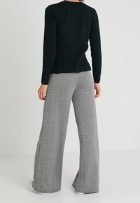 Czarny, teksturowany top z długim rękawem w połączeniu z szerokimi szarymi spodniami w kratę houndstooth. Lekki materiał, luźny krój, boczne rozcięcie w spodniach, gładkie białe buty.