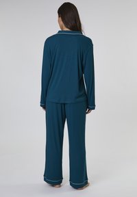 Set di pigiama teal realizzato in morbido tessuto, composto da una camicia a maniche lunghe con colletto e pantaloni larghi con dettagli in piping bianco.
