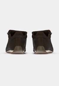 Ζευγάρι σκούρα καφέ casual παπούτσια, φαίνονται από πίσω, παρουσιάζοντας μαλακή υφή από σουέτ και υφασμένες μπεζ σόλες σε λευκό φόντο.