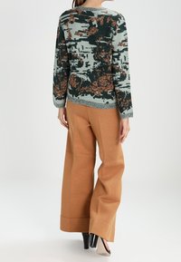 Zielono-pomarańczowy sweter w dzianinę z długimi rękawami, zestawiony z szerokimi beżowymi spodniami i czarno-kremowymi butami na słupku.