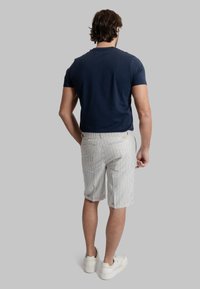 T-shirt di cotone blu navy e pantaloni corti a righe bianchi con linee blu. I pantaloni corti presentano tasche posteriori e orlo arrotolato. Sneakers bianche.