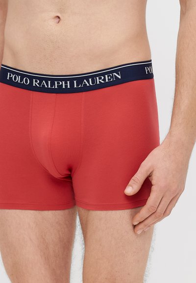 Raudonos tamprios medvilninės bokserinės trumpikės su tamsiai mėlynu liemeniu, ant kurio baltais rašmenimis parašyta „POLO RALPH LAUREN“, lygios tekstūros ir aptempto dizaino.