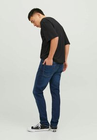 Jeans de mezclilla azul oscuro en un ajuste ceñido, combinados con una camiseta negra holgada y zapatillas negras. Costuras detalladas en los bolsillos.