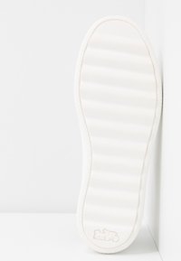 Semelle de chaussure en caoutchouc blanc avec des rainures horizontales et un logo en relief au talon, présentée sur un fond blanc en coin.