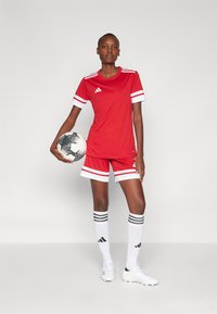 Rode voetbaluniform met een shirt met korte mouwen en witte gestreepte accenten, bijpassende shorts, witte sokken met zwarte strepen en een voetbal.