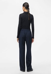 Top negro de manga larga combinado con pantalones holgados a rayas azules marinos. Los pantalones tienen una cintura elástica y un diseño de pierna recta.