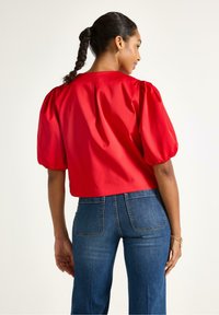 Rød satin crop top med puffede ærmer, parret med højtaljede blå denim jeans med baglommer og en lige pasform.