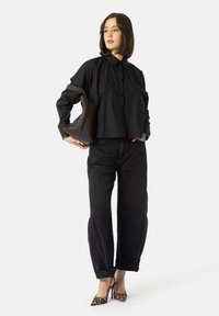 Černá košile s krátkým rukávem a uvolněným střihem, spárovaná s černými jeansy s vysokým pasem a leopardími lodičkami. Hnědá strukturovaná kabelka jako akcent.