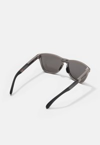 Ochelari de soare cu cadru din plastic gri și lentile gri închis. Au brațe texturate negre cu un accent de logo aproape de balama.