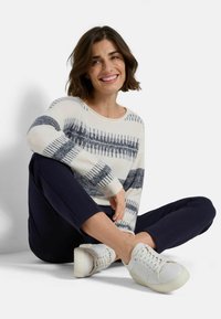 Maglione bianco con righe a motivo blu navy, scollatura rotonda e maniche lunghe. Abbinato a pantaloni blu navy e sneakers bianche con lacci.