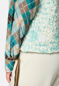 Knit sweater featuring a textured white and turquoise material. Sleeve patterned with blue, brown, and orange argyle. Logo patch on hem.